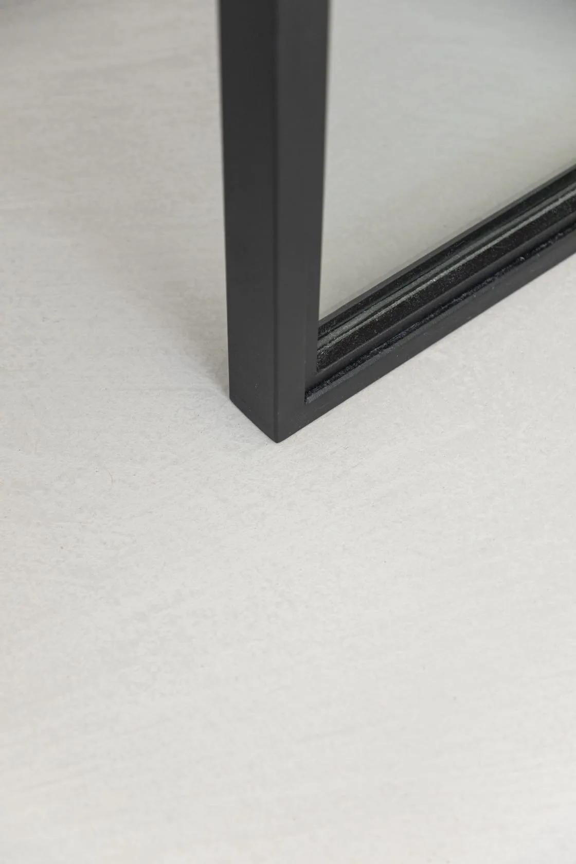 Détail d'un cadre en aluminium noir posé sur un sol en béton ciré gris clair